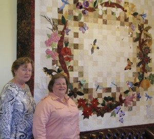Kathy Silvom (left) and Nancy Hiss stand in front of the group's wreath quilt.