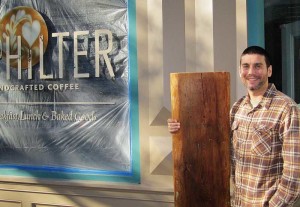 Chris Thompson, proprietor of Philter, a new coffee shop in Kennett Square, cradles a large slab of sculptured pine that soon will become a bench seat in the front window of the new shop he plans to open in late November.